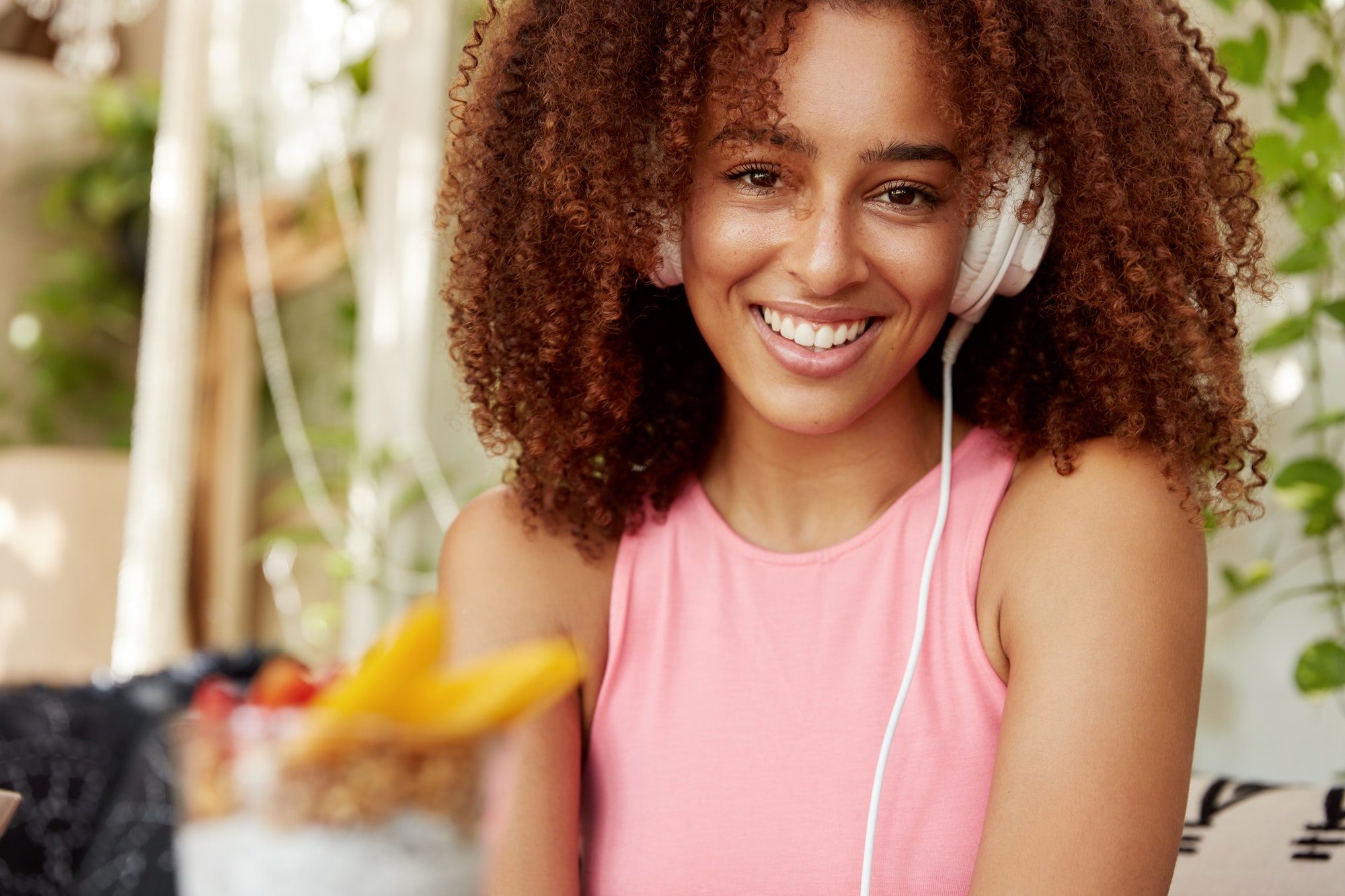 Afro American female student listens songs from playlist, enjoys perfect sound in modern headphones,